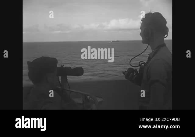 1944- Two sailors are shown at rail of ship; one looks through ...