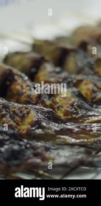 row of cooked fish in a row with a long wooden stick through its body ...