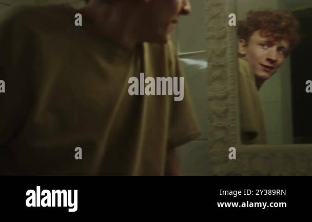 Young man turning between two mirrors in public bathroom looking in one ...