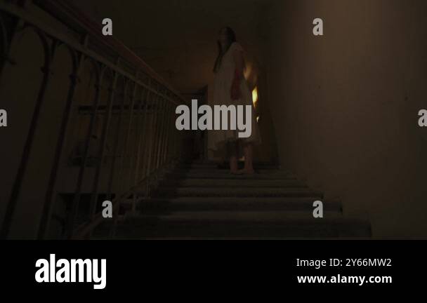 Young female on stairway in darkness. Creepy ghost woman in white dress ...