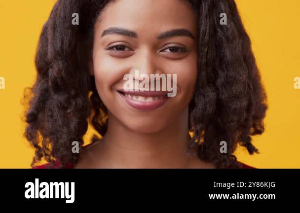 A young black woman with curly hair smiles brightly while standing ...