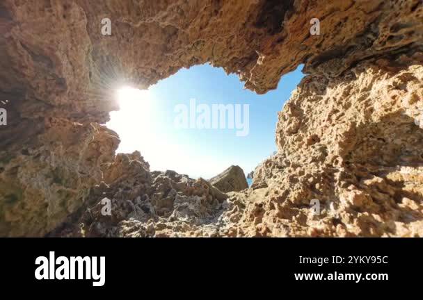 Zoom out, A bright sunbeam shines through a jagged rock opening ...