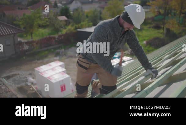Construction worker securing wooden beams on rooftop with hammer, side ...