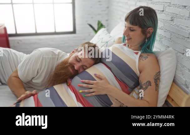 Man and woman lie on bed in bedroom with man listening to woman's ...