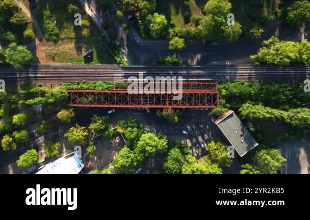 Rusty railway bridge passing above train tracks in lush green urban ...
