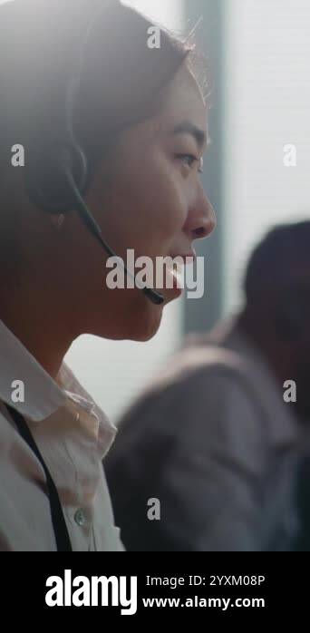 Vertical shot of Asian helpline operator in headset having conversation ...