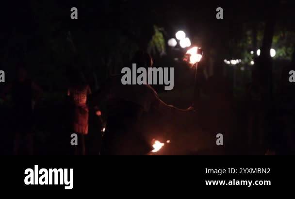 woman twists a long rope with a flame at the end and throws it far in ...