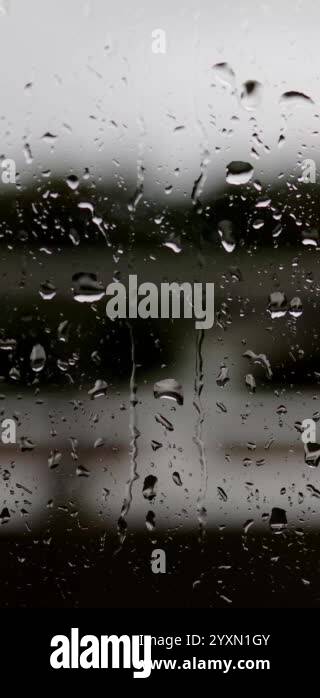 Portrait footage of rain drops rolling down a window on a hotel balcony ...