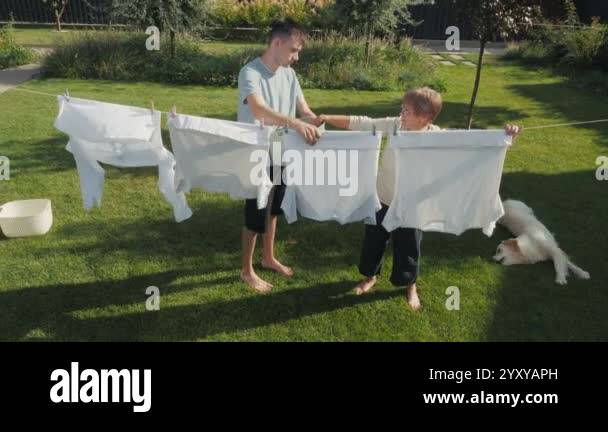 Picture of A young man and an older woman hang white laundry on a clothesline in a ...