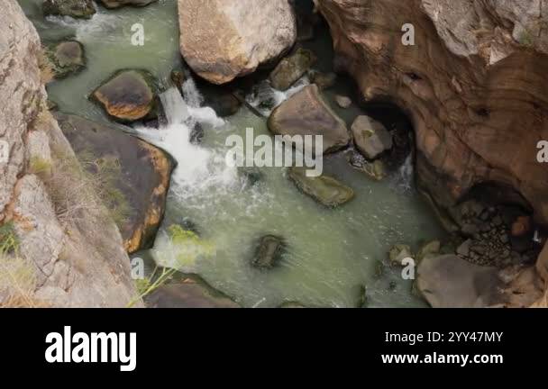 Picture of Clear water cascades over stones in a rocky canyon, surrounded by ...