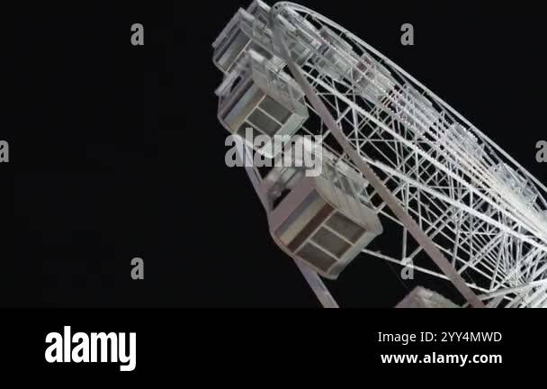 Ferris wheel rotating at an amusement park at night. White metal spokes ...
