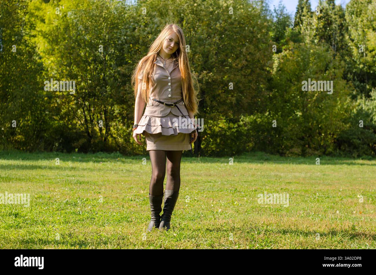 Young woman with long red hair walks through sunlit park. Wearing beige ...
