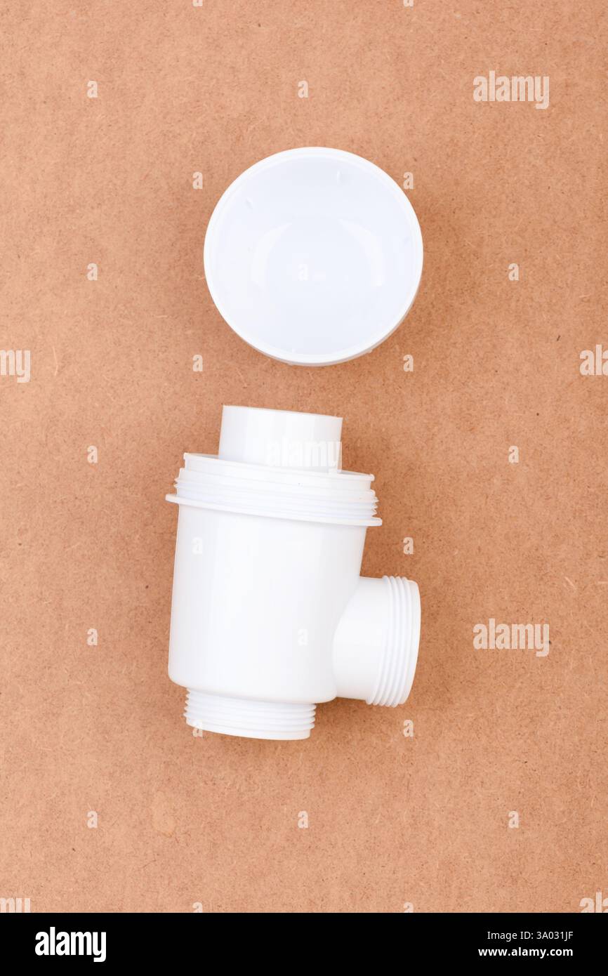 White plastic sink drain trap with threaded ends and open plug placed on brown surface. Stock Photo