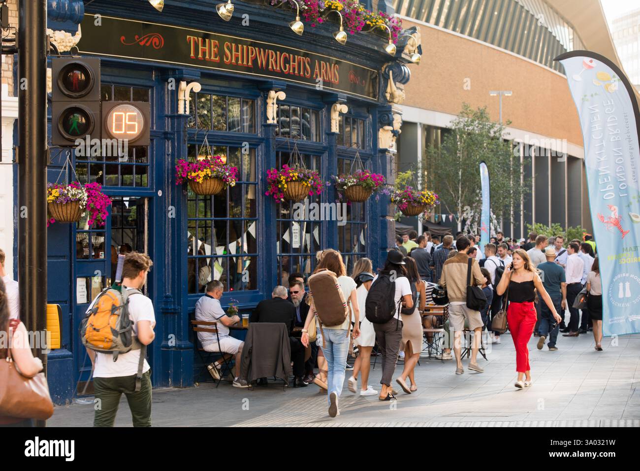 Pedestrians cross near the Shipwrights Arms pub, London, UK.  Pedestrian crossing signal shows 05 seconds remaining.  Outdoor seating and a food festi Stock Photo