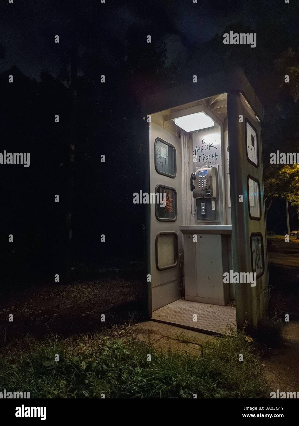 Brightly lit open pay-phone booth (public telephone booth), alone in the dark night; concept of desolate, creepy, uncanny, spooky - Smartphone Captured Stock Image