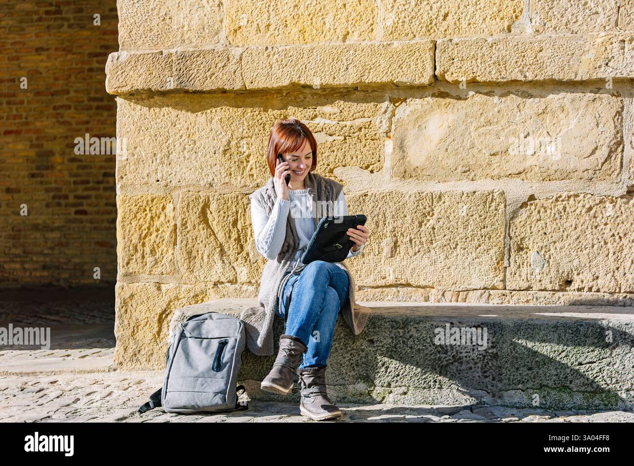 Woman working remotely on tablet while talking on phone outdoors. Lifestyle. Technology. Stock Photo