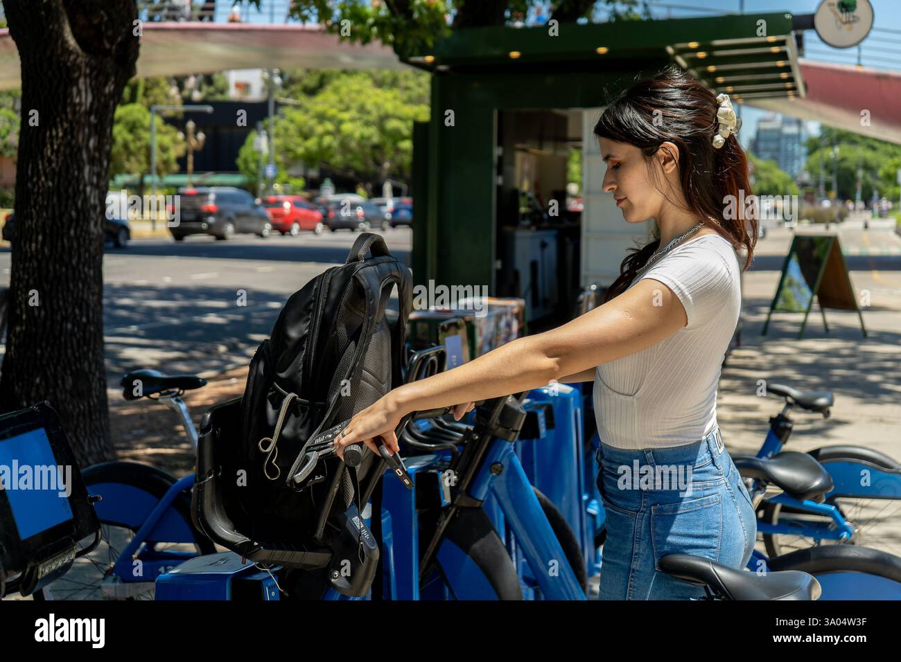 Elegant young woman putting her backpack on a public bike, getting ...