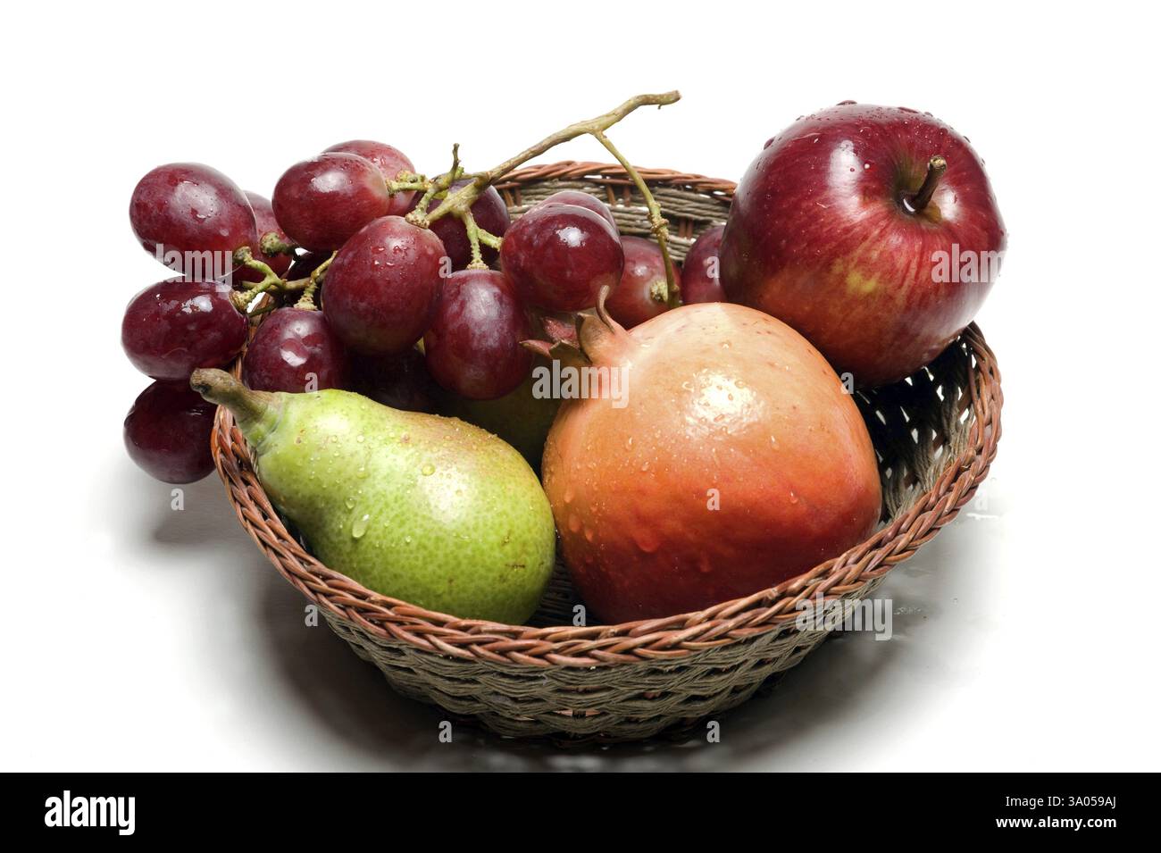 Fruits, water drops on apple, pomegranate, pear and grapes in wooden basket on white background Stock Photo