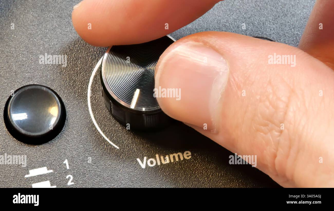 Hand adjusting a volume knob on an audio device, close-up of fingers turning a sound control dial, music loudness setting simple concept, detail close Stock Photo