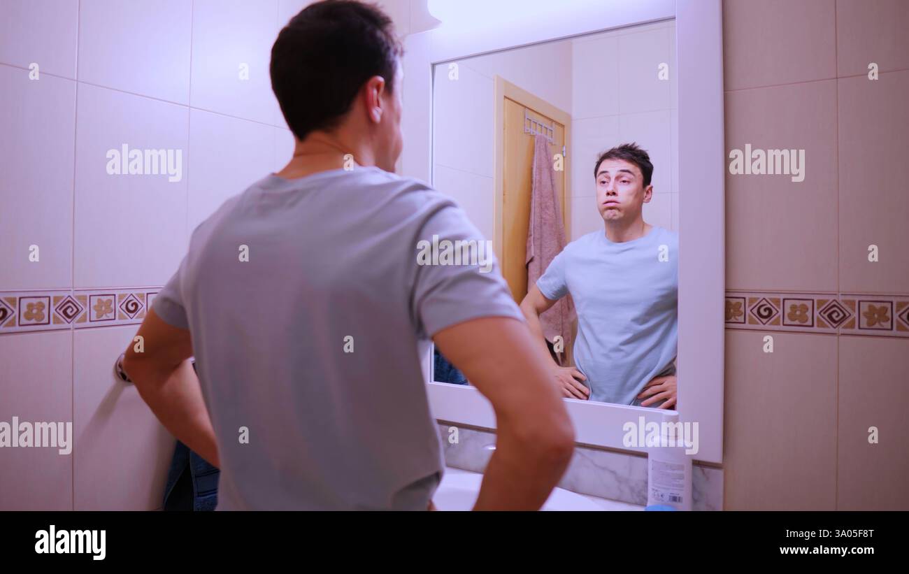 Sleepy man looking at mirror in bathroom before work Stock Photo