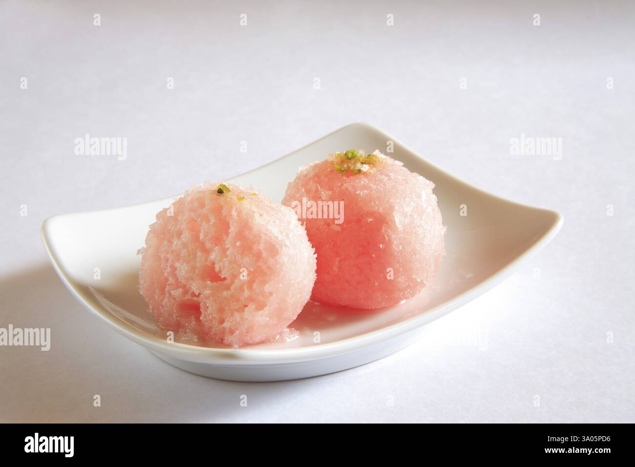 One and half piece of bengali mithai raskadam garnish with coconut and pistachio in rectangle plate on white background Stock Photo