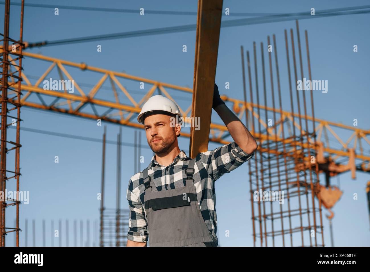 Against crane. With wooden plank. Man is working on the construction site at daytime. Stock Photo