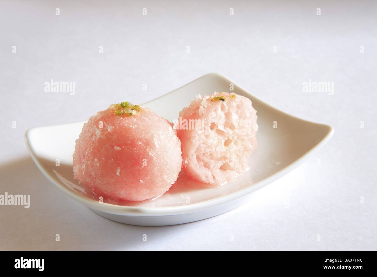 One and half piece of bengali mithai raskadam garnish with coconut and pistachio in rectangle plate on white background Stock Photo