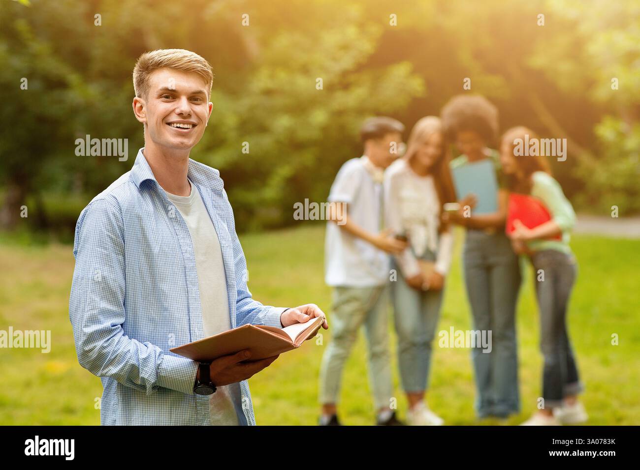 Student Guy Preparing For Exam Outdoor While His Friends Chatting On Background Stock Photo