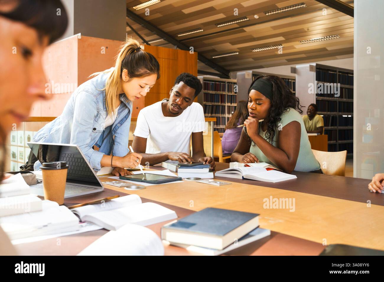 Multiracial friends discussing assignment over digital tablet at desk in university library Stock Photo