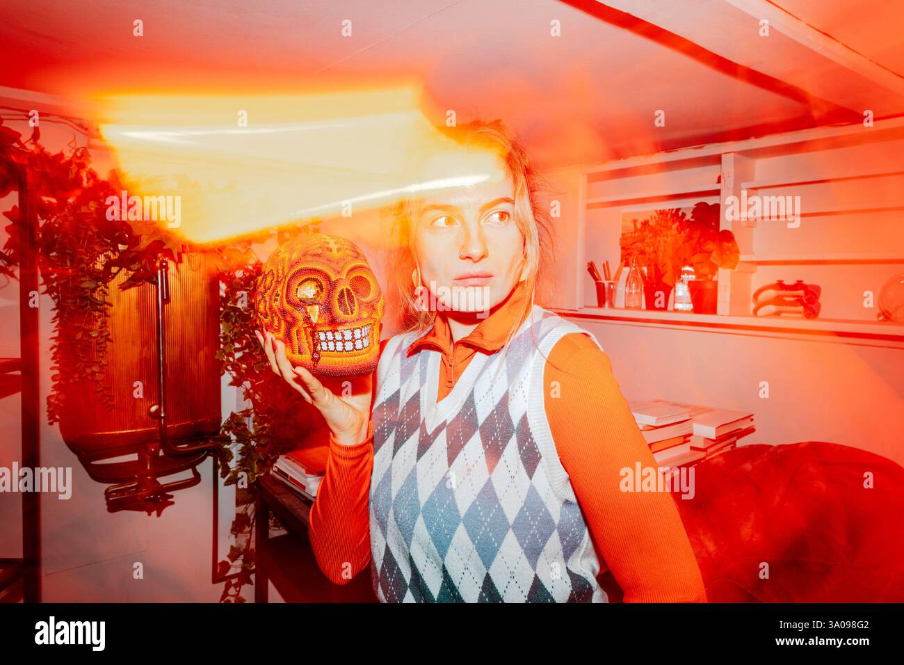 Businesswoman holding artificial human skull and looking away amidst bright orange lights Stock Photo