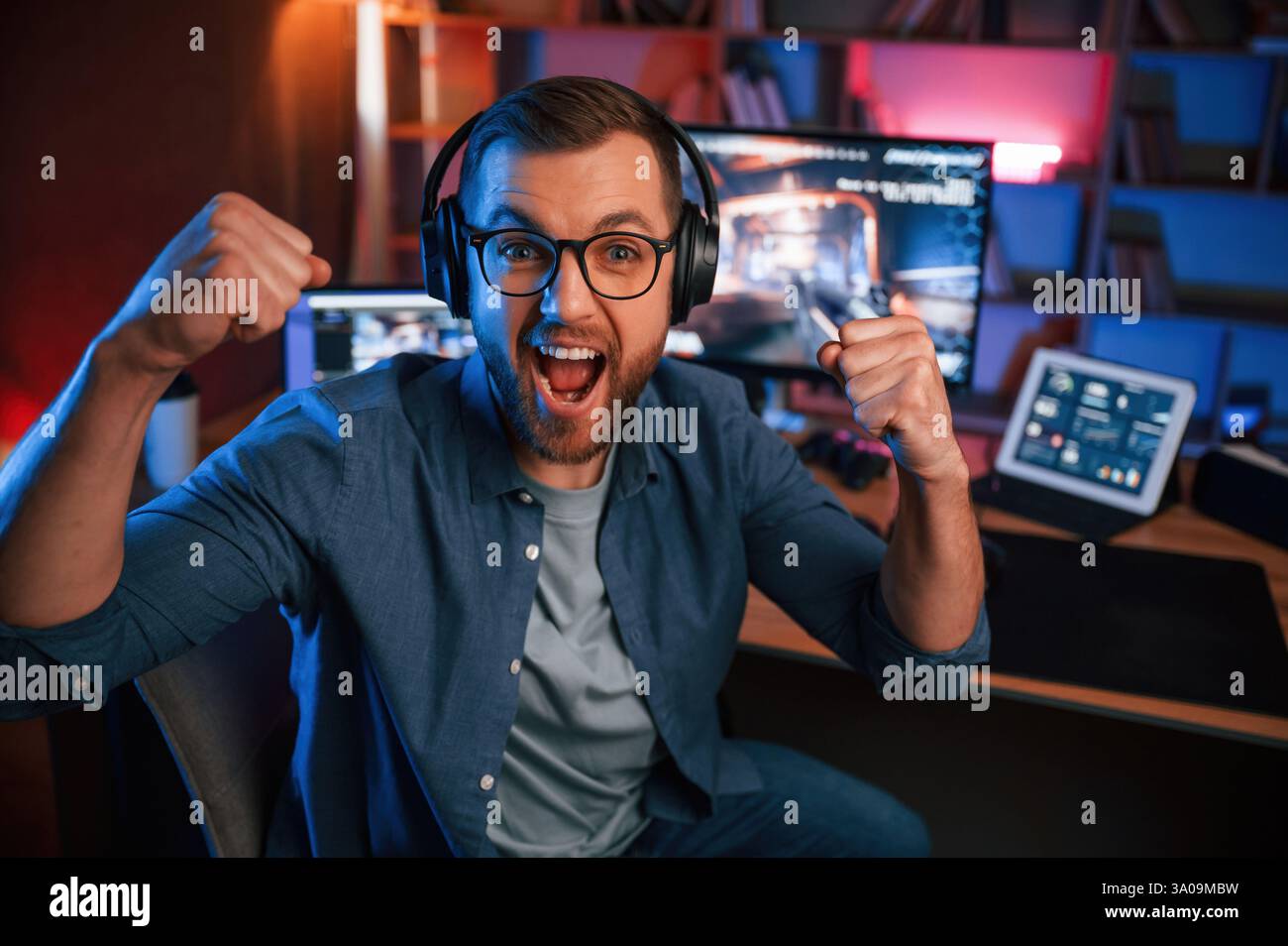 Uplifting and energized man is playing the shooter game on his computer. Neon lighting. Stock Photo