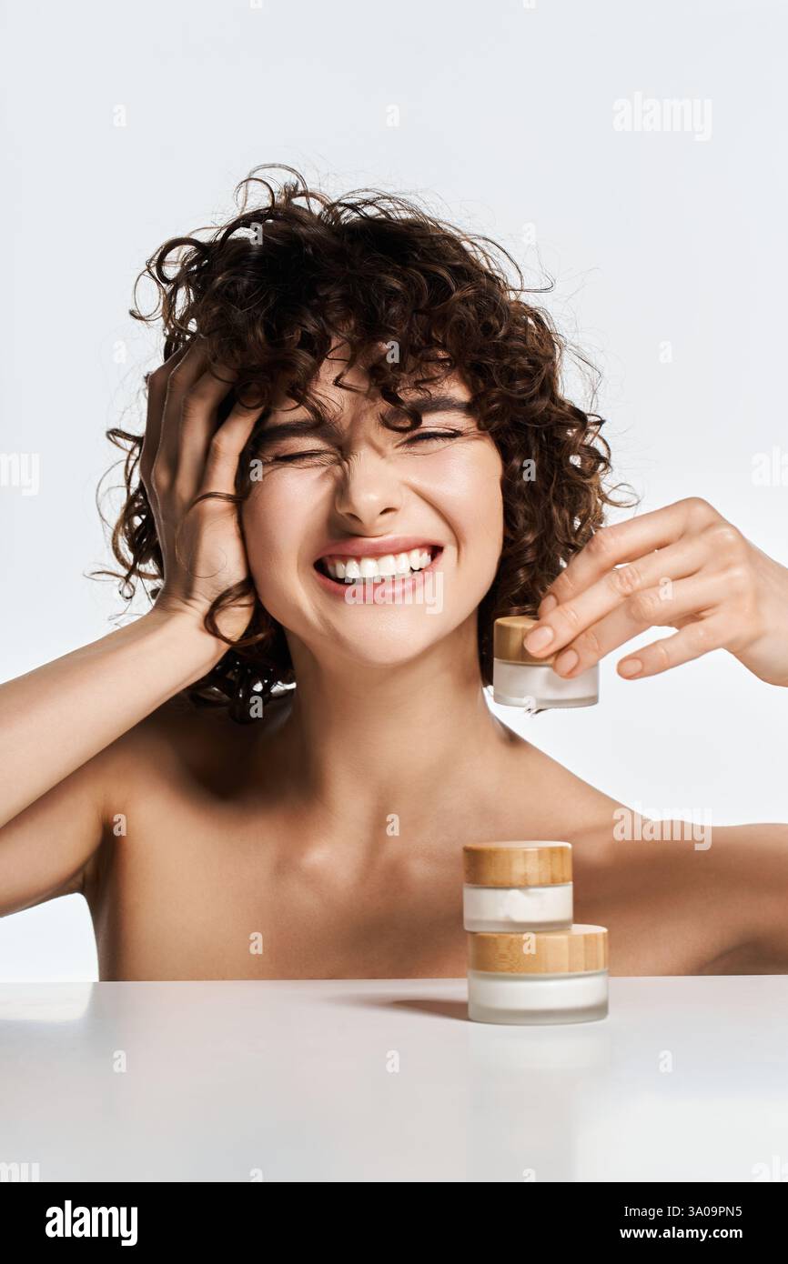 Joyful young woman smiles while holding a skincare jar, embodying beauty and confidence. Stock Photo