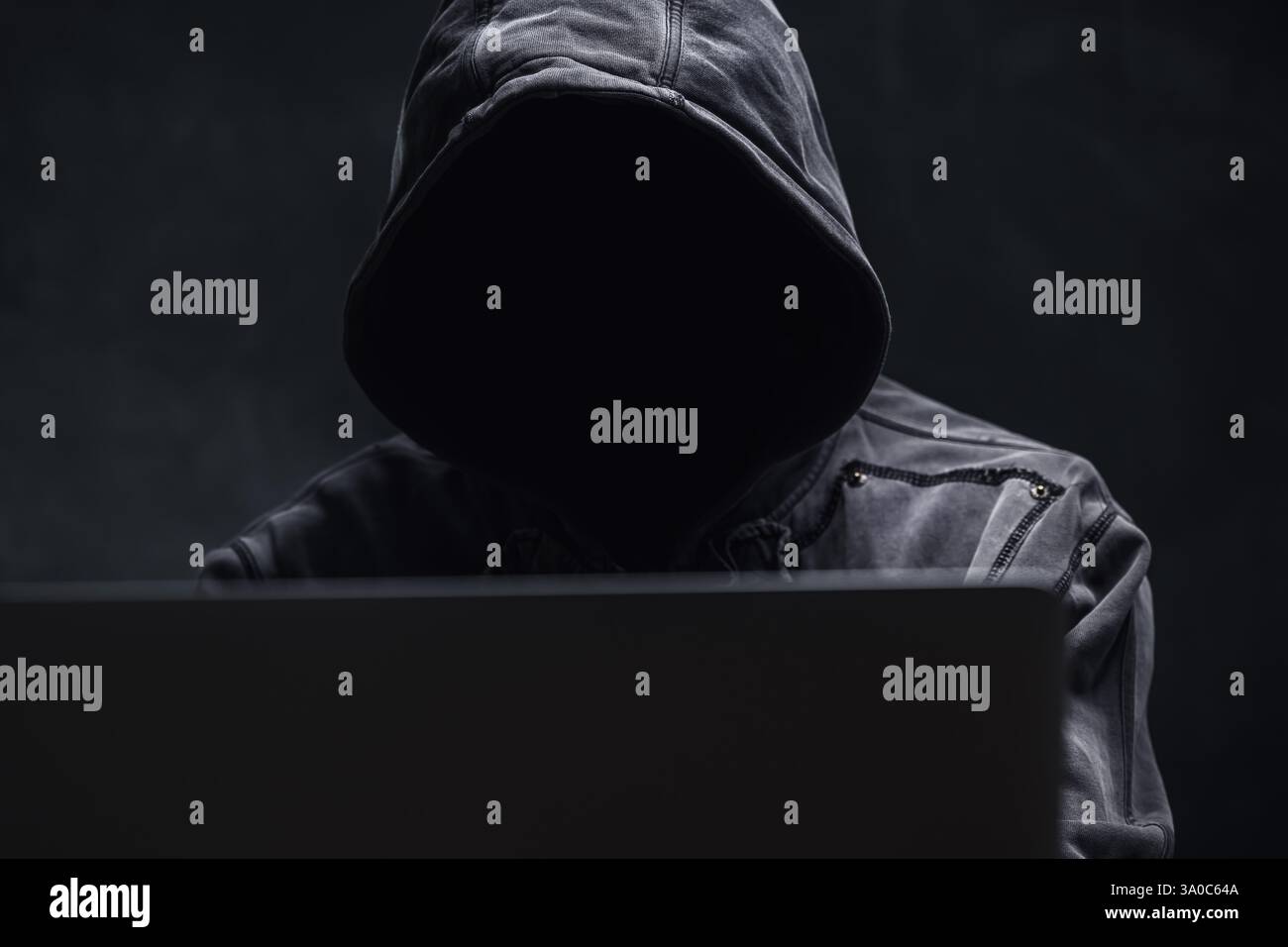 Hooded computer hacker using laptop computer, selective focus Stock Photo