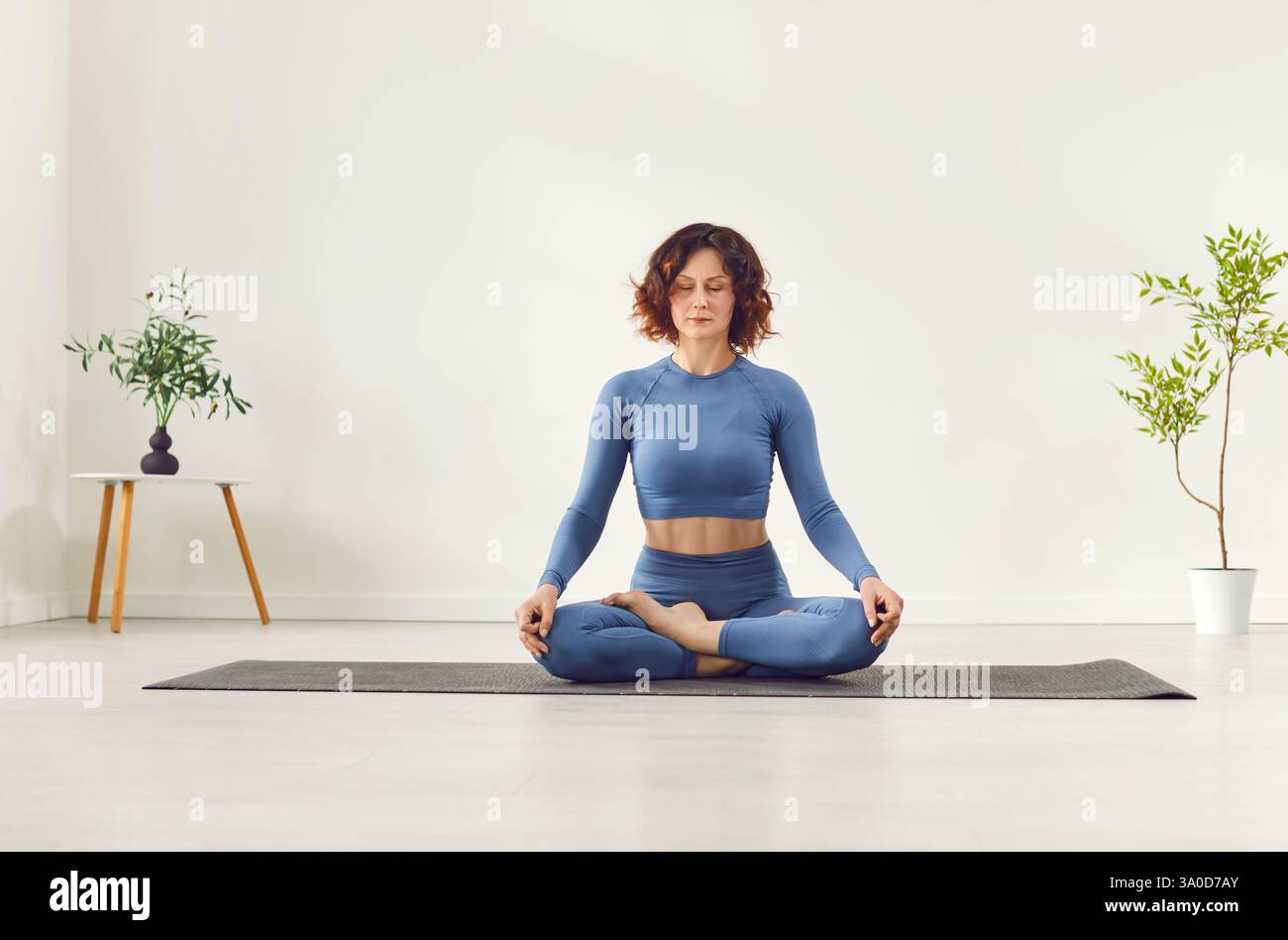 Yogi sporty attractive woman practicing yoga, doing Ardha Padmasana exercise, meditating in Half Lotus  Stock Photo