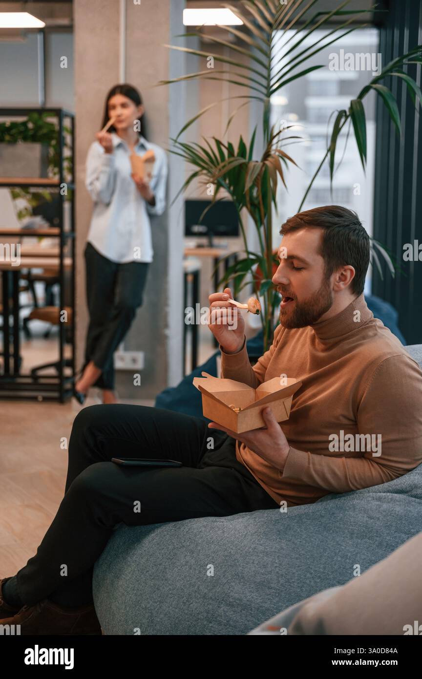 Office workers are in the rest zone is having a break and eating food from paper eco boxes. Stock Photo