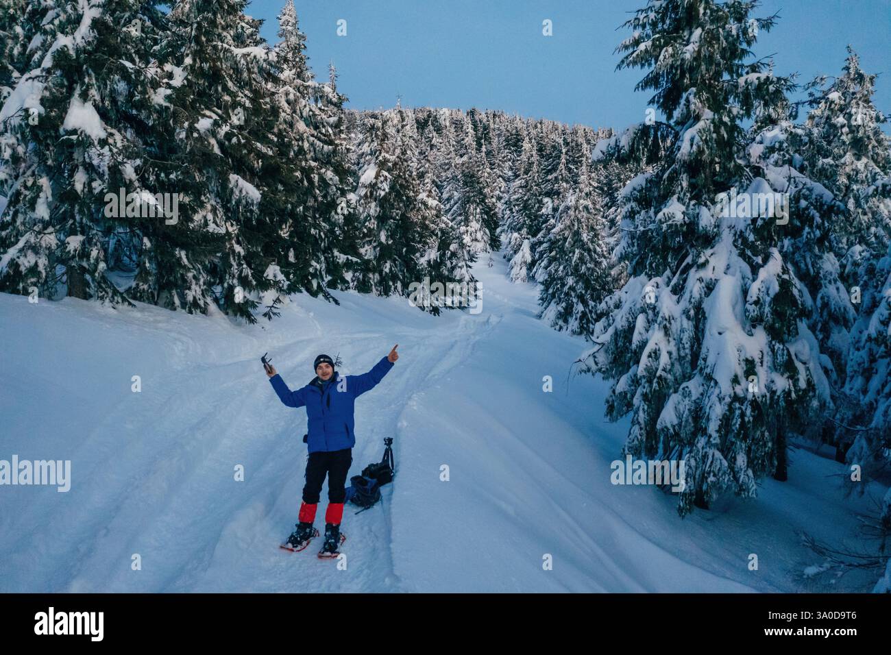 Man in snowshoes is standing, holding drone controller. In the majestic forest of Carpathian mountains. Stock Photo