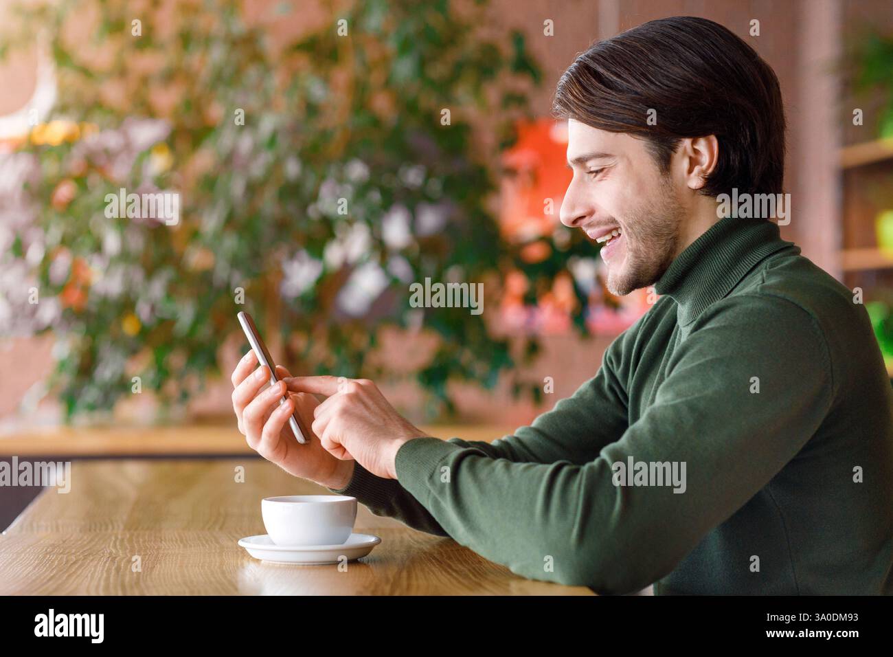 Young man using smartphone while drinking coffee at cafe Stock Photo