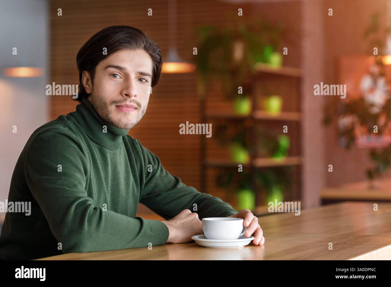 Young handsome man sitting alone at cafe, drinking coffee Stock Photo