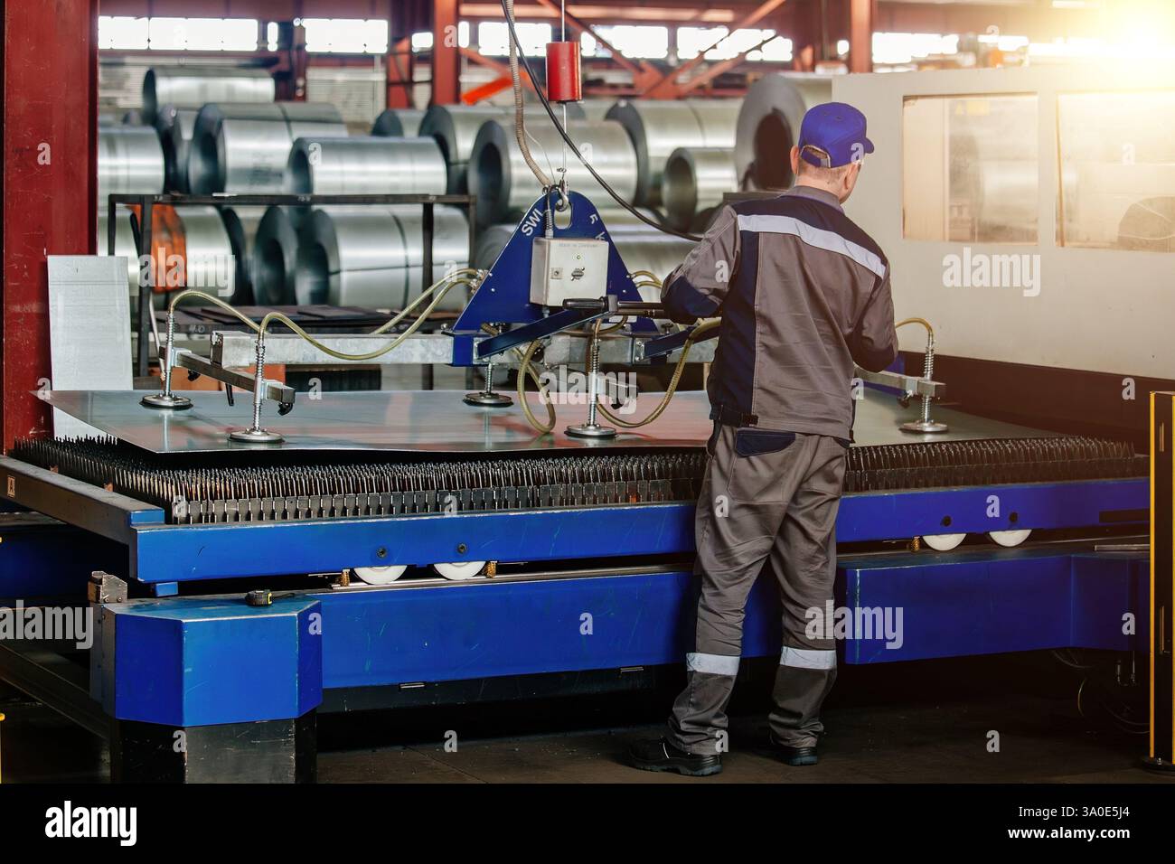Worker operates mechanical vacuum lifter in metalworking factory. Stock Photo