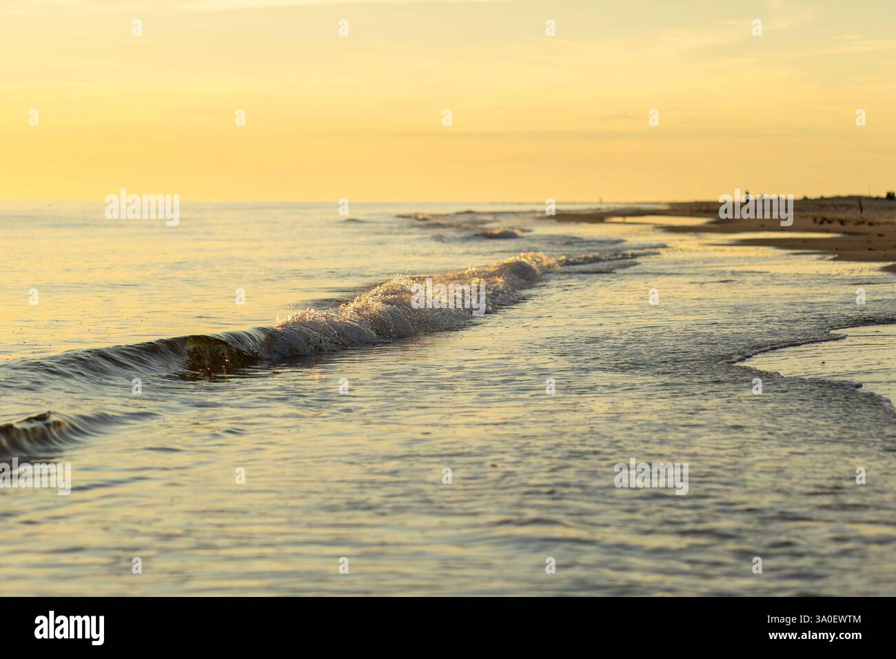 The setting sun casts a warm glow over the calm ocean, while gentle ...