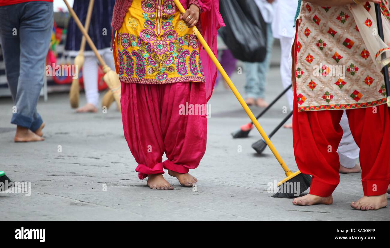 Barefoot women wearing traditional indian clothes are sweeping the street during a religious procession, showcasing their devotion and community servi Stock Photo