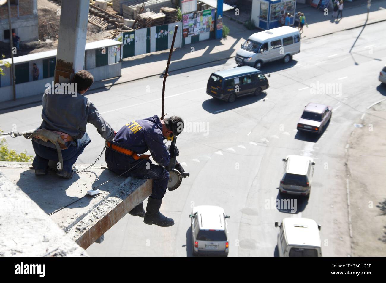 Two construction workers in safety gear work on the edge of a high-rise ...