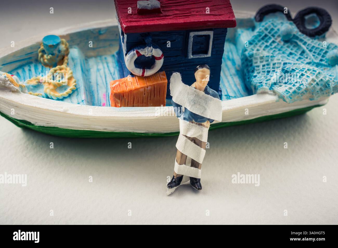 Tiny wrapped figurine of man model beside a model boat Stock Photo