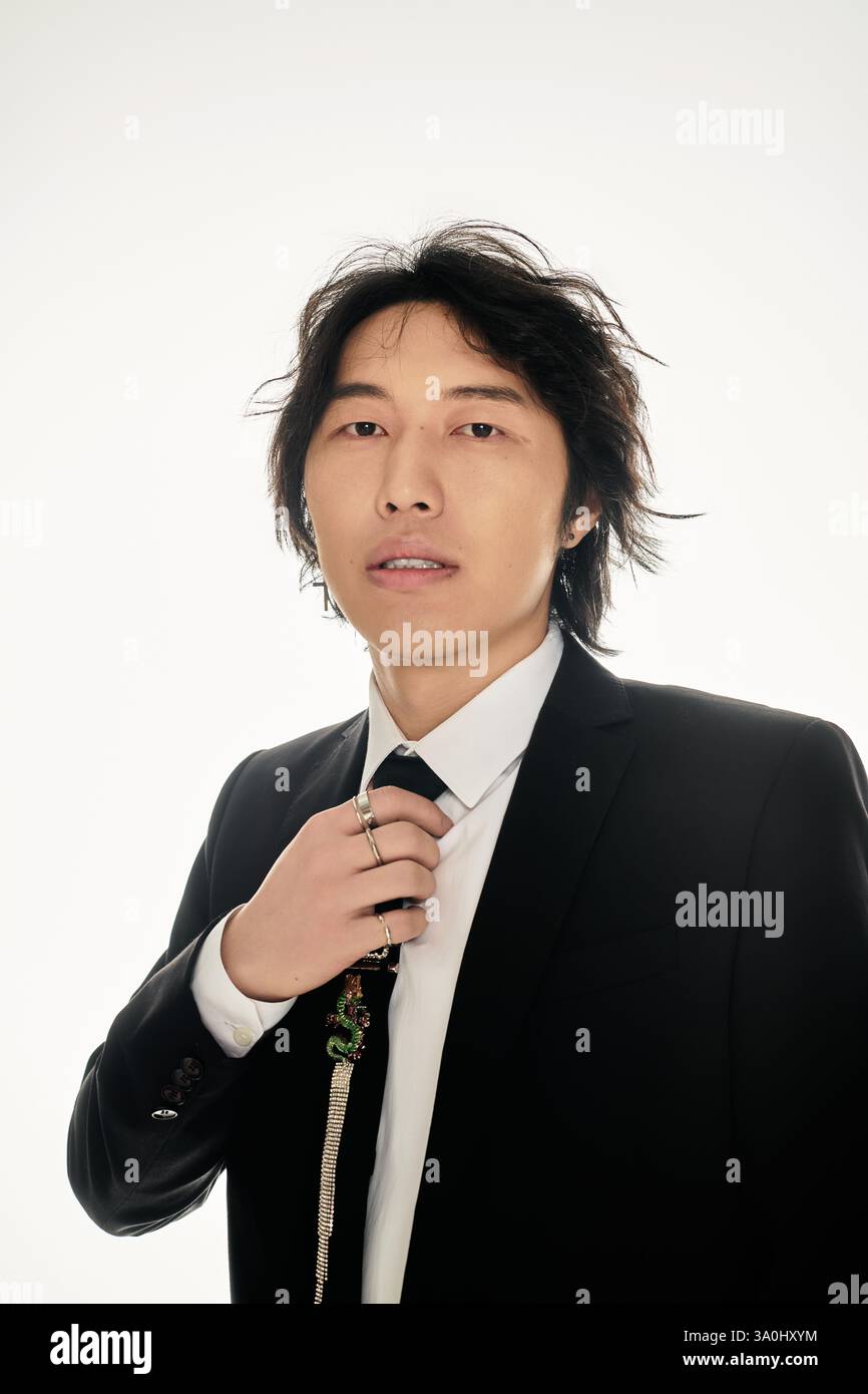 Handsome young asian man dressed in a sharp suit adjusts his tie with ...