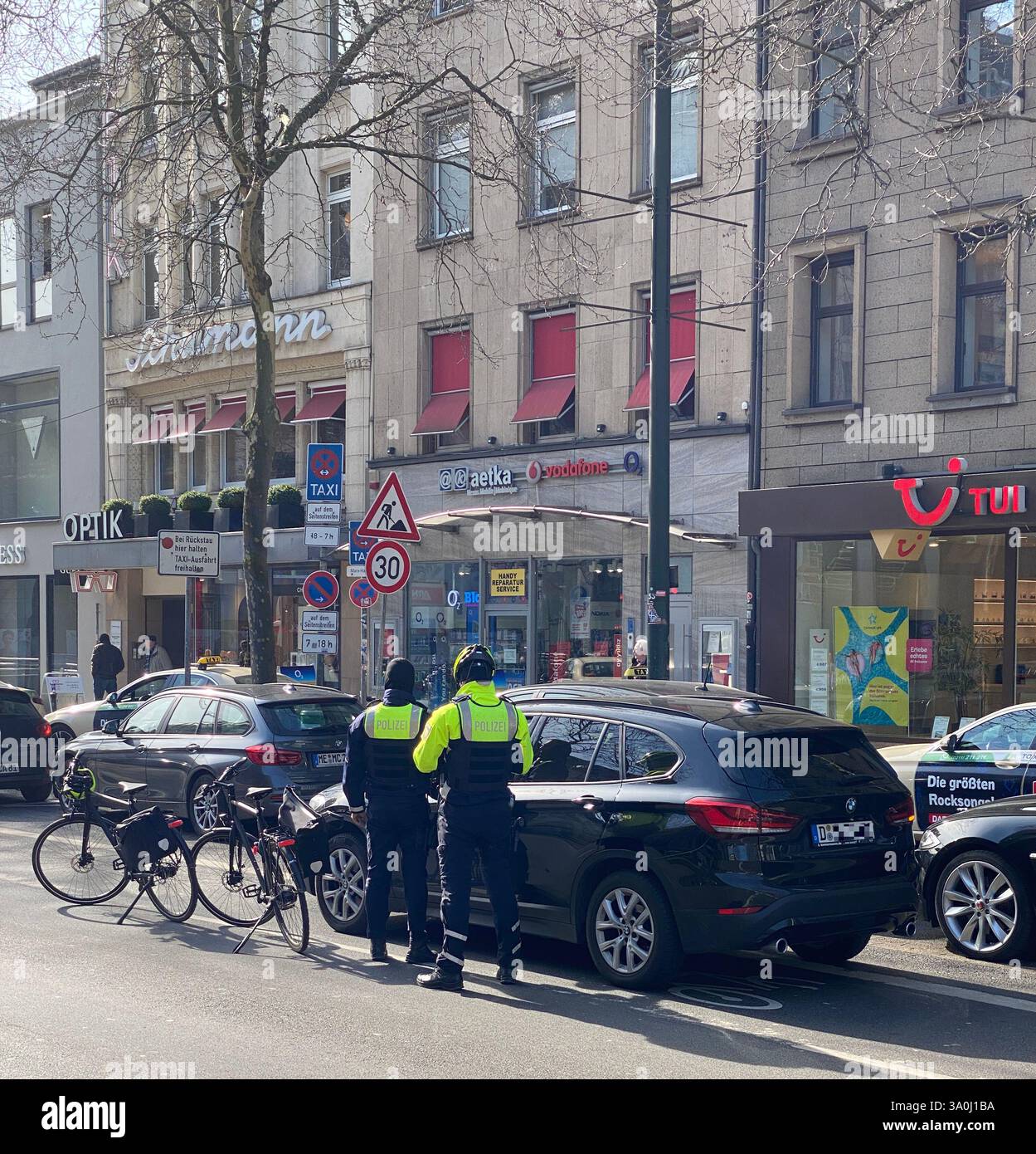 Zwei Fahrradpolizisten kontrollieren ein Fahrzeug, das auf dem Fahrradweg angehalten hat. Die Polizisten sind selbst mit Fahrrädern in der Innenstadt. - Smartphone Captured Stock Image