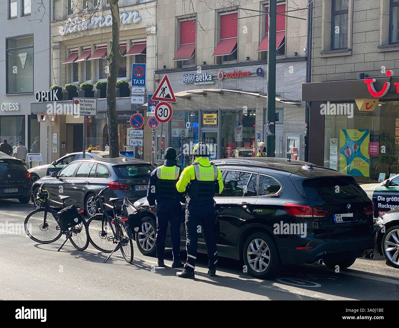 Zwei Fahrradpolizisten kontrollieren ein Fahrzeug, das auf dem Fahrradweg angehalten hat. Die Polizisten sind selbst mit Fahrrädern in der Innenstadt. - Smartphone Captured Stock Image