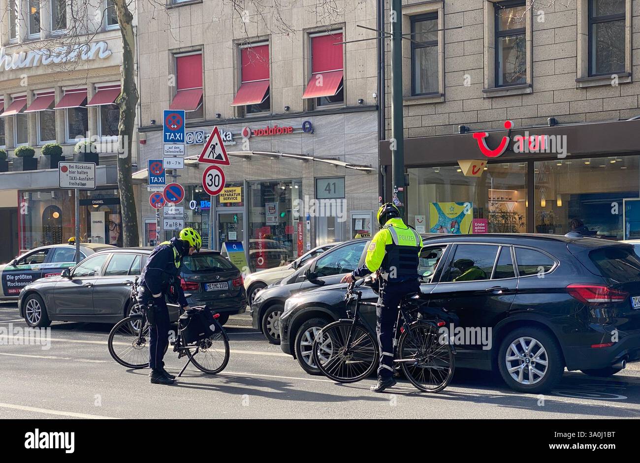 Zwei Fahrradpolizisten kontrollieren ein Fahrzeug, das auf dem Fahrradweg angehalten hat. Die Polizisten sind selbst mit Fahrrädern in der Innenstadt. - Smartphone Captured Stock Image