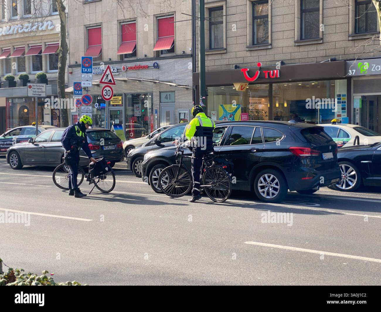 Zwei Fahrradpolizisten kontrollieren ein Fahrzeug, das auf dem Fahrradweg angehalten hat. Die Polizisten sind selbst mit Fahrrädern in der Innenstadt. - Smartphone Captured Stock Image