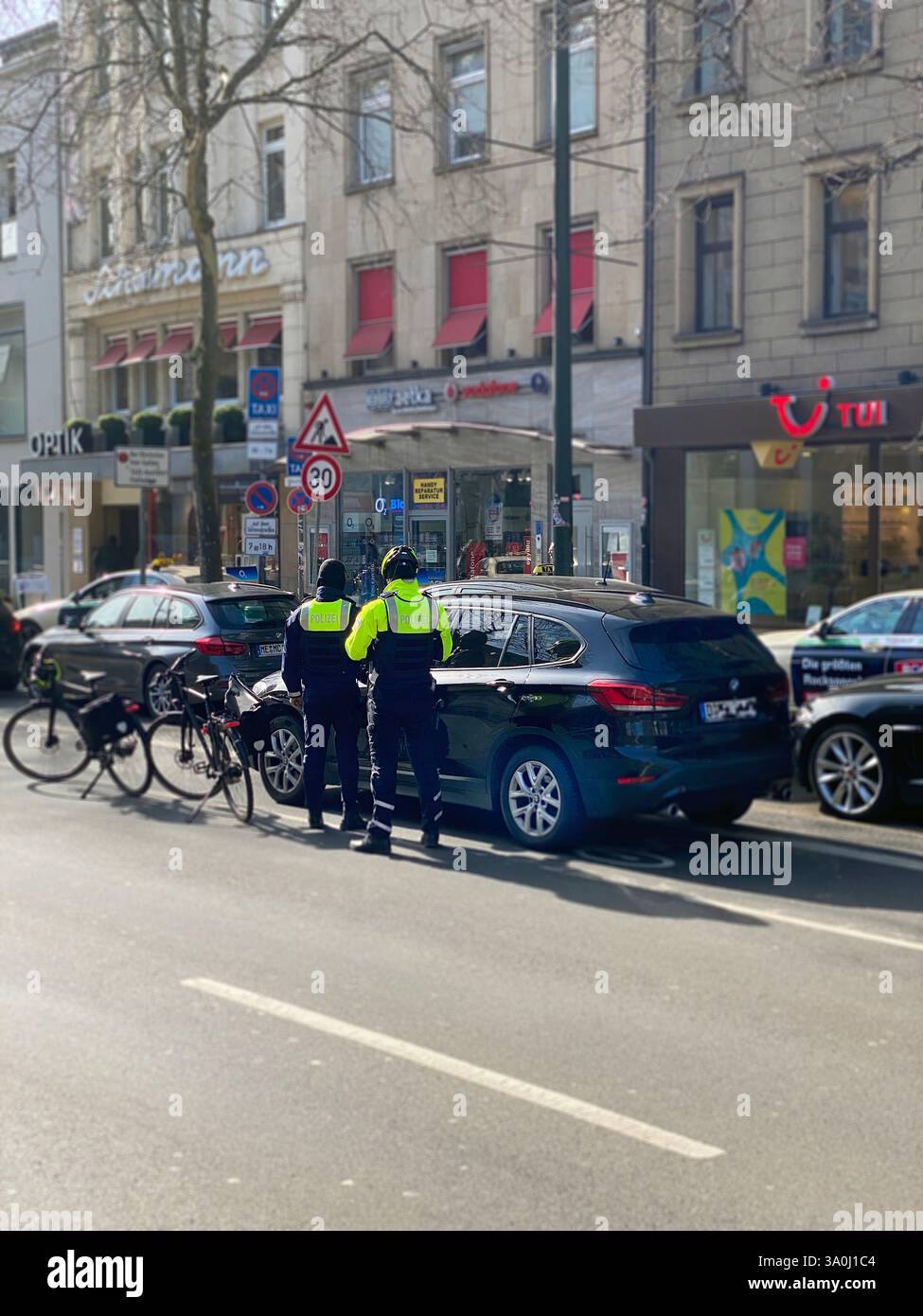 Zwei Fahrradpolizisten kontrollieren ein Fahrzeug, das auf dem Fahrradweg angehalten hat. Die Polizisten sind selbst mit Fahrrädern in der Innenstadt. - Smartphone Captured Stock Image