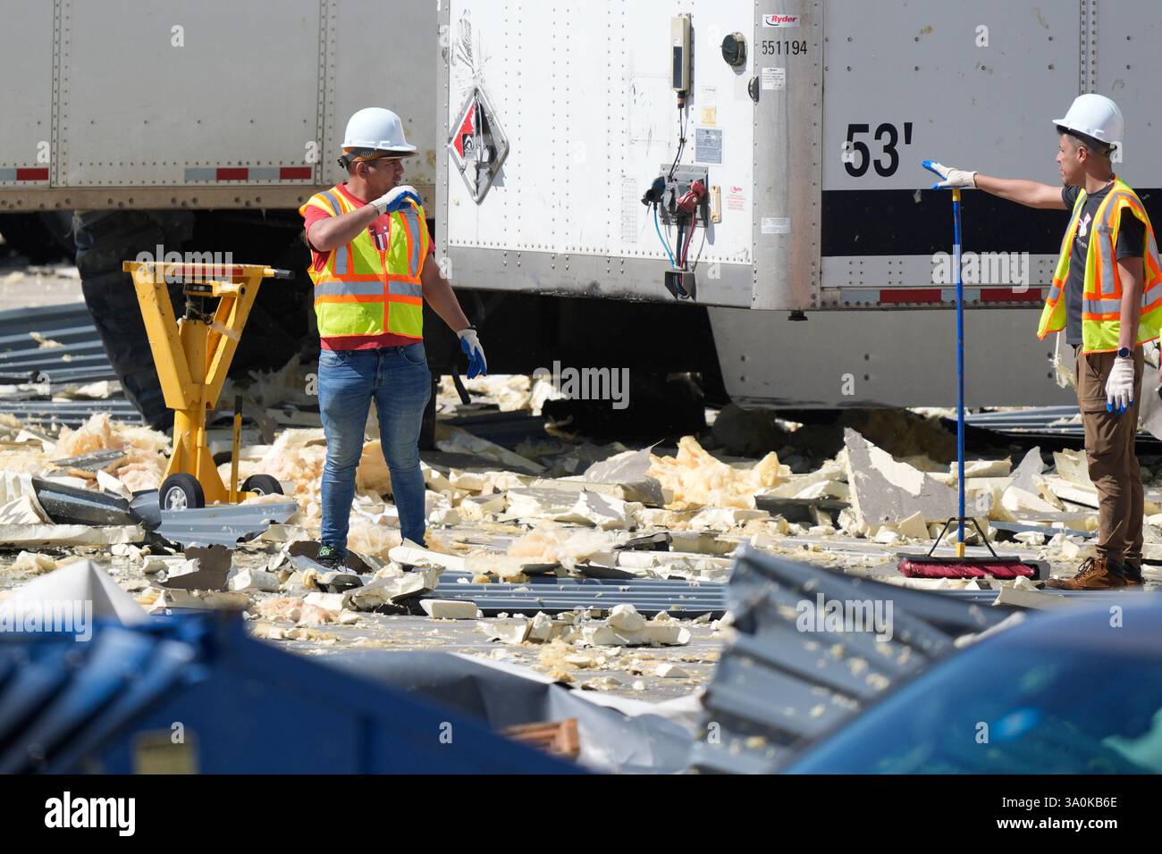 Workers talk while cleaning up debris from a damaged warehouse after ...